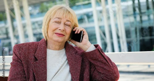 Beautiful older woman speaks on the phone outdoors in the sunlight near the business center photo