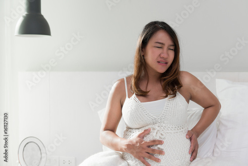 Photos Pregnant women with tummy-ache which lying on bed in home