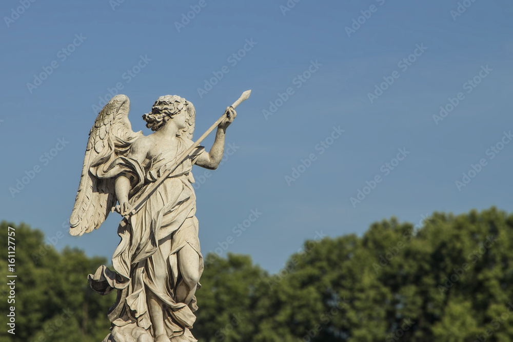 Roman sculpture of woman high above with blurred trees in the background and bright landmark with tall carving.  Copyspace.