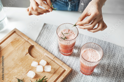 Close up of girl's hands decorating grapefruit detox healthy smoothie with rosemary.