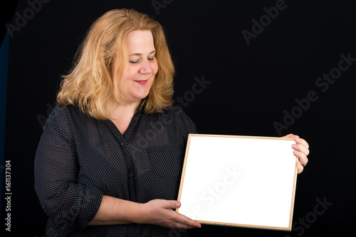 Beautiful light overweighted european red haired adult carrying a white blank board in front of a black background - studio shot