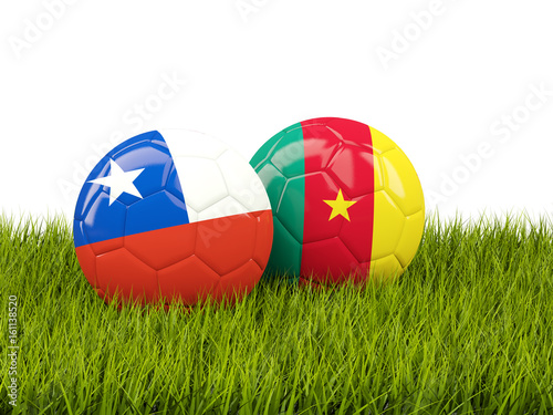 Two footballs with flags of Chile and Cameroon on green grass