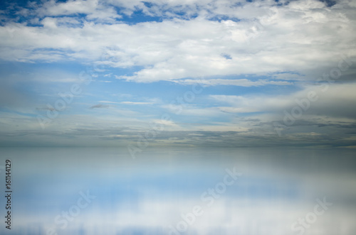 Blue sky. Dramatic clouds over sea. Blurred reflection of sky in water