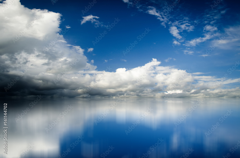 Blue sky. Dramatic clouds over sea. Blurred reflection of sky in water