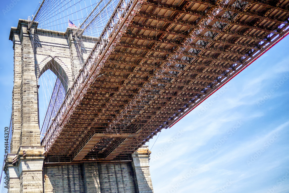 Fototapeta premium Underside of the Brooklyn Bridge as seen from Brooklyn Bridge Park across the East River from Manhattan.