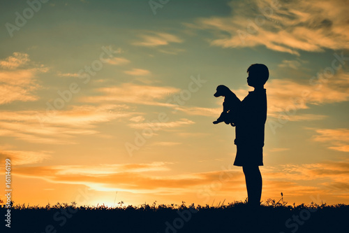 Silhouette boy playing with little dog on the sky sunset color of vintage tone