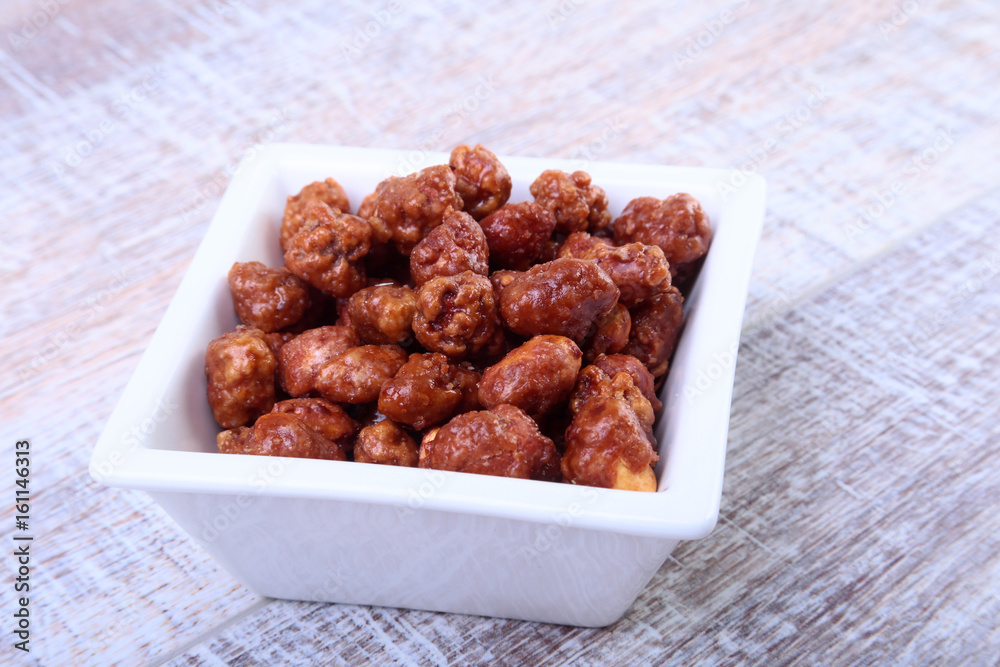Sugared Hazelnuts in a white bowl on a wooden background. Hazelnuts in sugar glaze. Selective focus. Sugared Hazelnuts in a white bowl on a wooden background. Hazelnuts in sugar glaze. Selective focus.