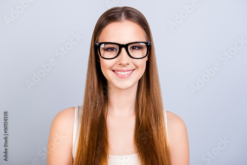 Cute young female student is in a stylish black glasses, wearing casual singlet, smiling, standing on pure light background with long hair photo