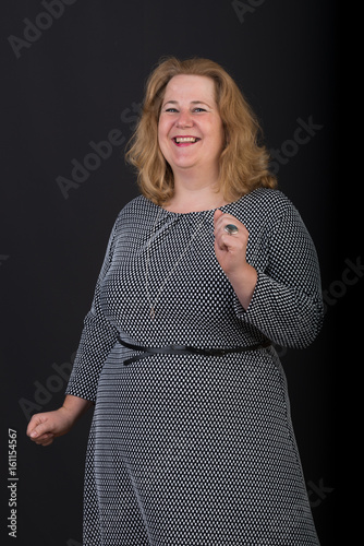 Portrait of a attractive european light overweighted red haired female in grey black dotted dress, happy dancing alone, half body studio shot