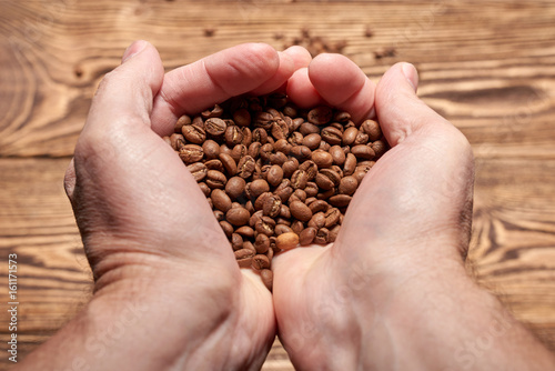Human hand holding roasted brown coffee beans over rustic wooden background