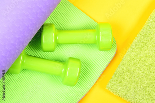 Dumbbells on green and purple yoga mat and towel
