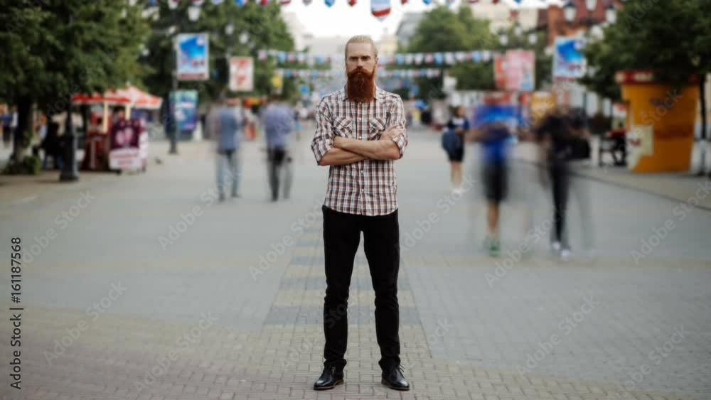 Timelapse of Young bearded man standing still at sidewalk in crowd traffic stream with people moving fast