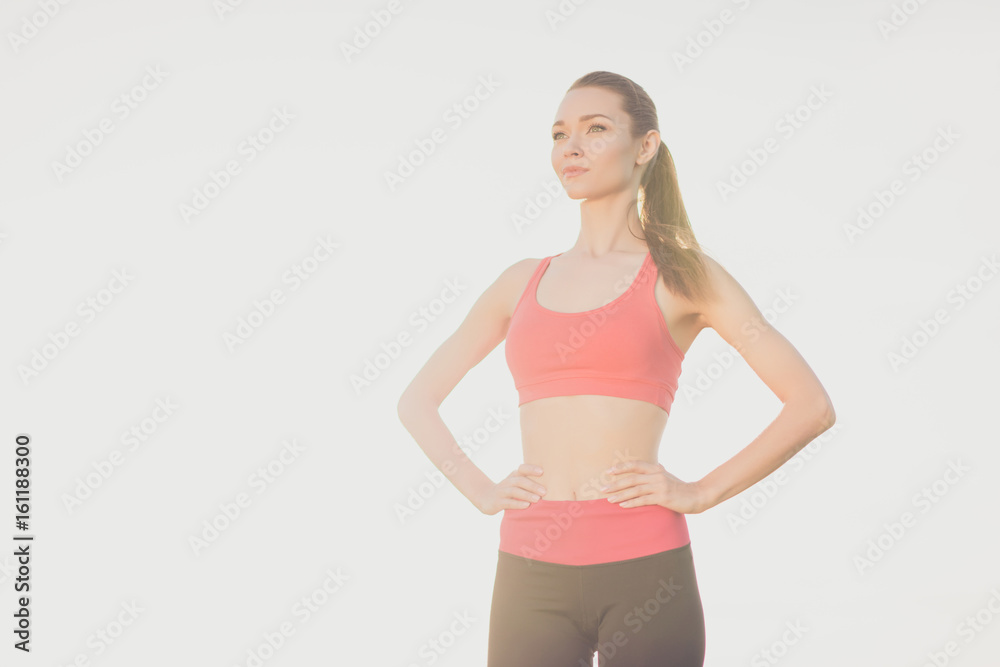 Attractive fit sportgirl with hands on waist is ready for work out. She is wearing stylish sport wear, pony tail, stands isolated on white background, looks healthy and slim Attractive fit sportgirl with hands on waist is ready for work out. She is wearing stylish sport wear, pony tail, stands isolated on white background, looks healthy and slim