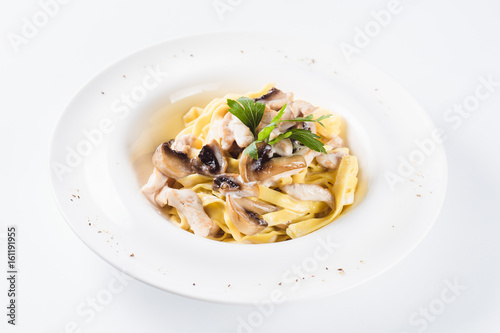 Pasta with chicken and mushrooms on a round white plate on a light background (close)