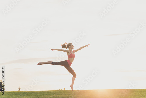 Freedom and happiness. Young gymnast in fashion sportswear is jumping in graceful pose on the sunset background, in a spring park outdoors