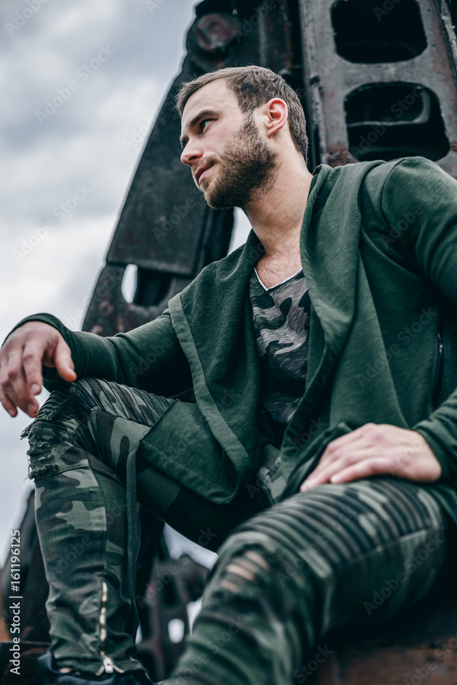 Portrait of a young handsome bearded man, model of fashion, in clothes khaki colors. Man on city of urban rusty background. Portrait of a young handsome bearded man, model of fashion, in clothes khaki colors. Man on city of urban rusty background.