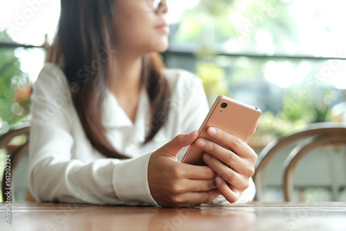 asia woman holding mobile phone sitting and waiting for someone in coffee cafe. image for business,people,portrait,mobile and technology concept