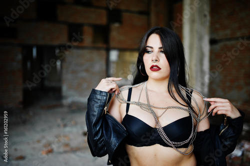 Brunette plus size sexy woman with earring in the nose, wear at black leather jacket, lace  bra at abadoned place.