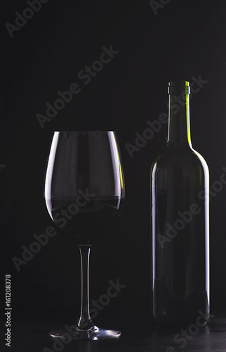 Cup and empty wine bottle on black background.