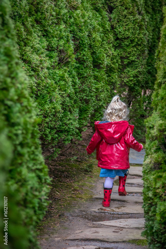 Small girl in raincoat running down a garden path