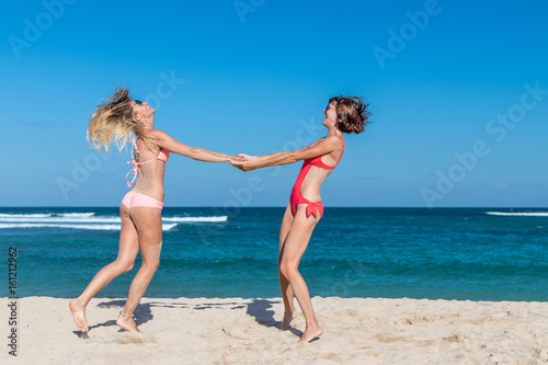 Two happy female friends having fun and swirling on the tropical beach of Bali island, Nusa Dua, Indonesia.