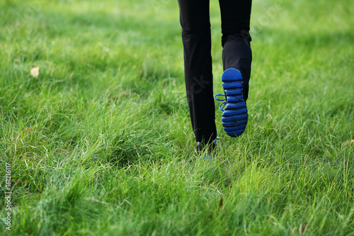 Woman steps on green grass, sport blue sole shoes, black pant, healthy lifestyle, lower half