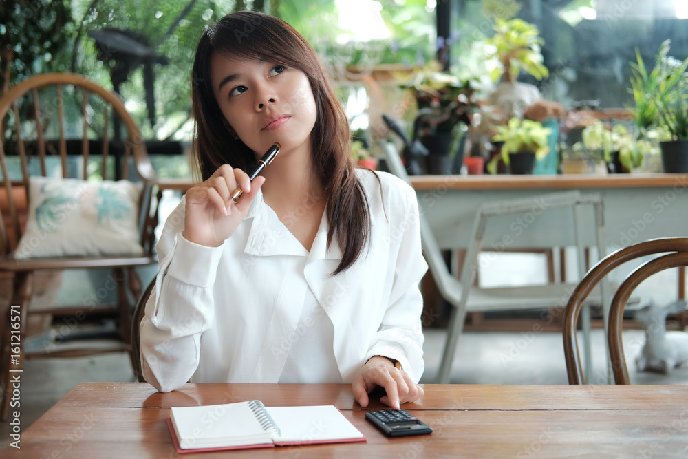 young student woman holding with pen and thinking of something have notebook paper,calculator putting on front of her. image for business,education,people,portrait and emotion concept young student woman holding with pen and thinking of something have notebook paper,calculator putting on front of her. image for business,education,people,portrait and emotion concept