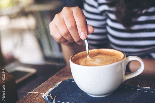 A woman holding coffee spoon and stirring hot coffee on wooden table