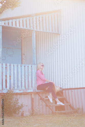 Fototapeta Naklejka Na Ścianę i Meble -  Young beautiful blonde girl is sitting on the stairs at home. Rest on the ranch, outside the city.