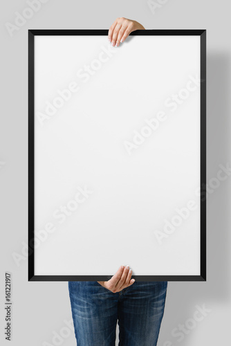 Woman holding a blank poster with black frame mockup isolated on a gray background. 