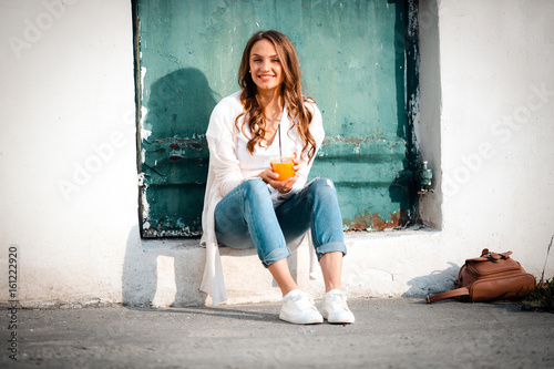 Smiling beautiful woman holding cup orange juice, sitting outdoo