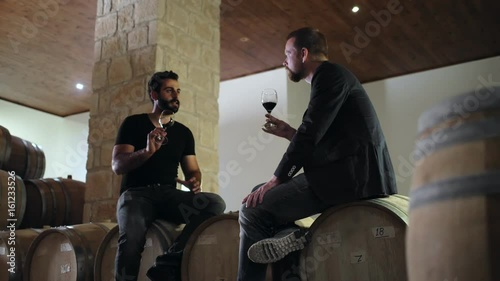 Serious men taste a new batch of wine in the wine cellar photo
