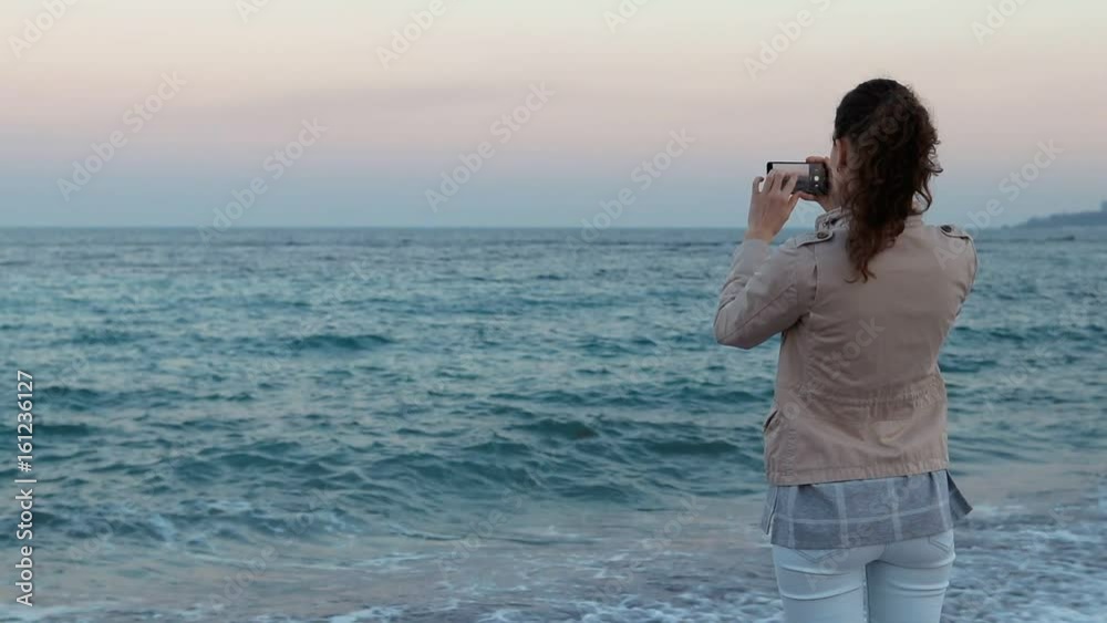 Young woman on the beach taking pictures of the ocean on a mobile phone, slow motion Young woman on the beach taking pictures of the ocean on a mobile phone, slow motion