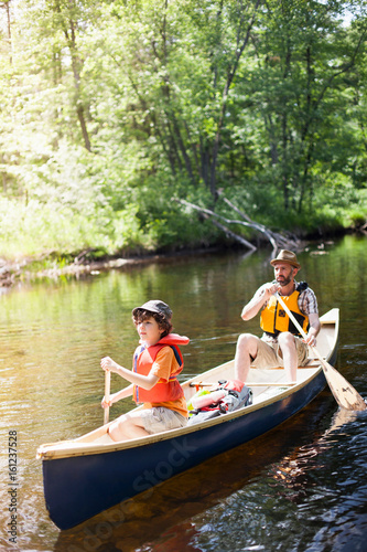 Father and son paddling canoe on river