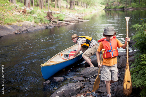 Father and son pushing canoe in river