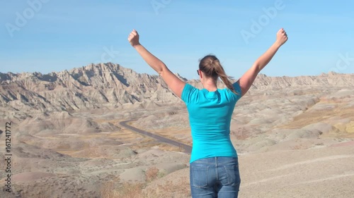 Wallpaper Mural SLOW MOTION: Female tourist hiking Badlands National park and victoriously raising her arms up, overlooking pointy sandstone mountains on sunny day. Cheerful woman celebrating reaching mountaintop Torontodigital.ca