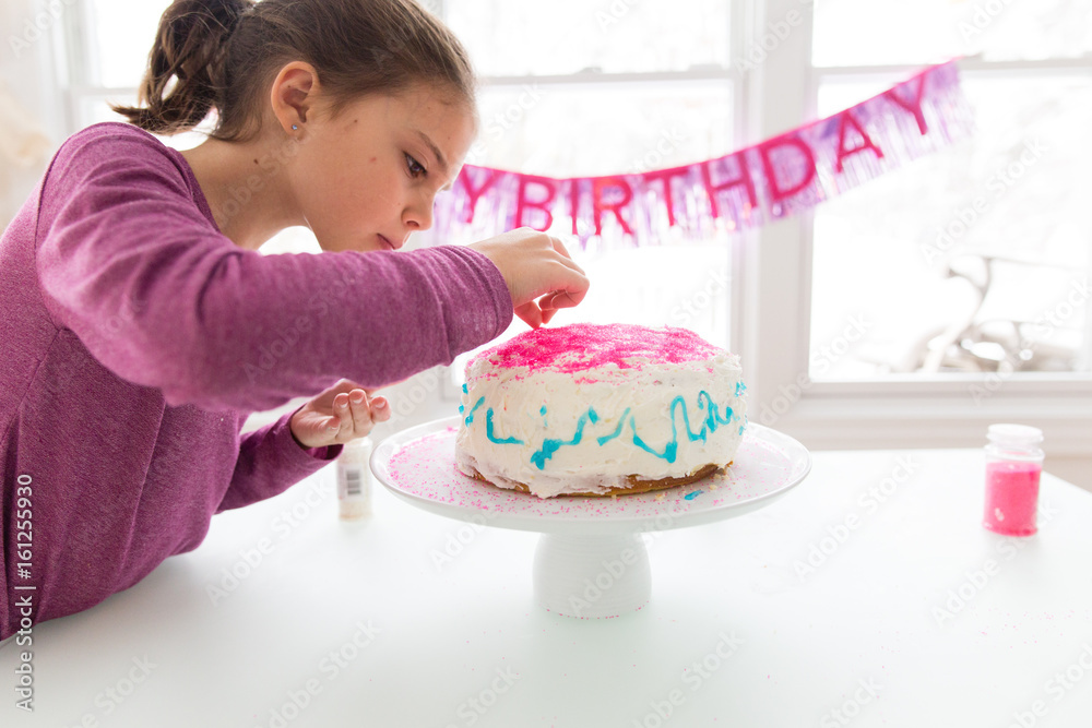 Girl decorating birthday cake with sprinkles Girl decorating birthday cake with sprinkles