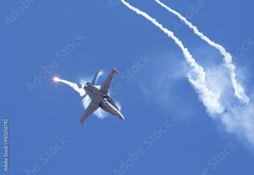 Modern tactical jet fighter shooting flares. White smoke  missiles against a blue sky. Focus point on the aircraft.