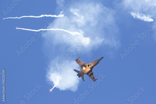 Modern tactical jet fighter shooting flares. White smoke, missiles against a blue sky. Focus point on the aircraft. photo