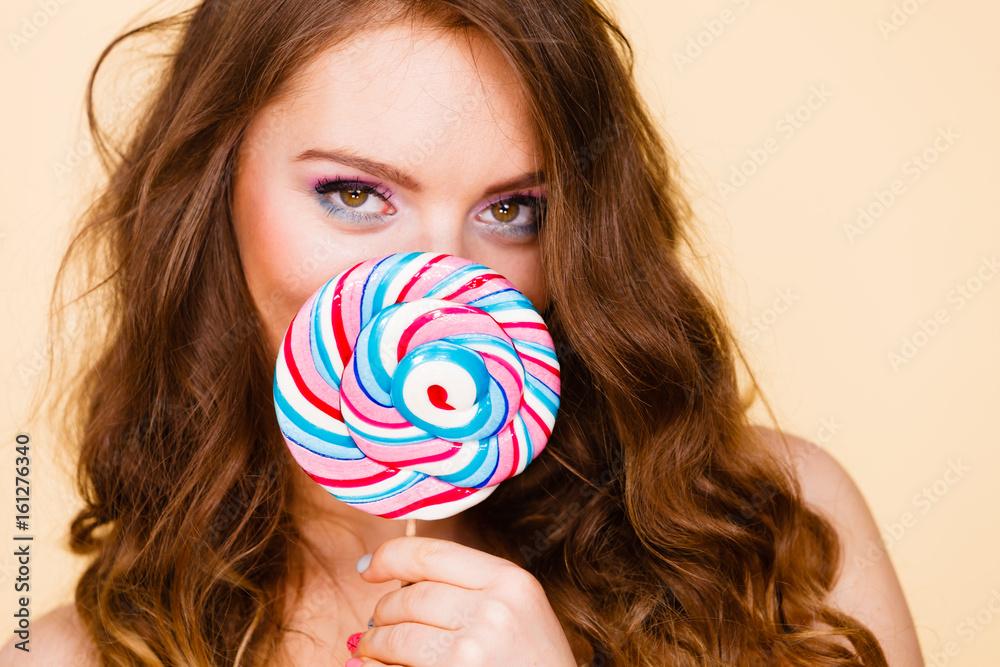 Woman holds colorful lollipop candy in hand, covering face