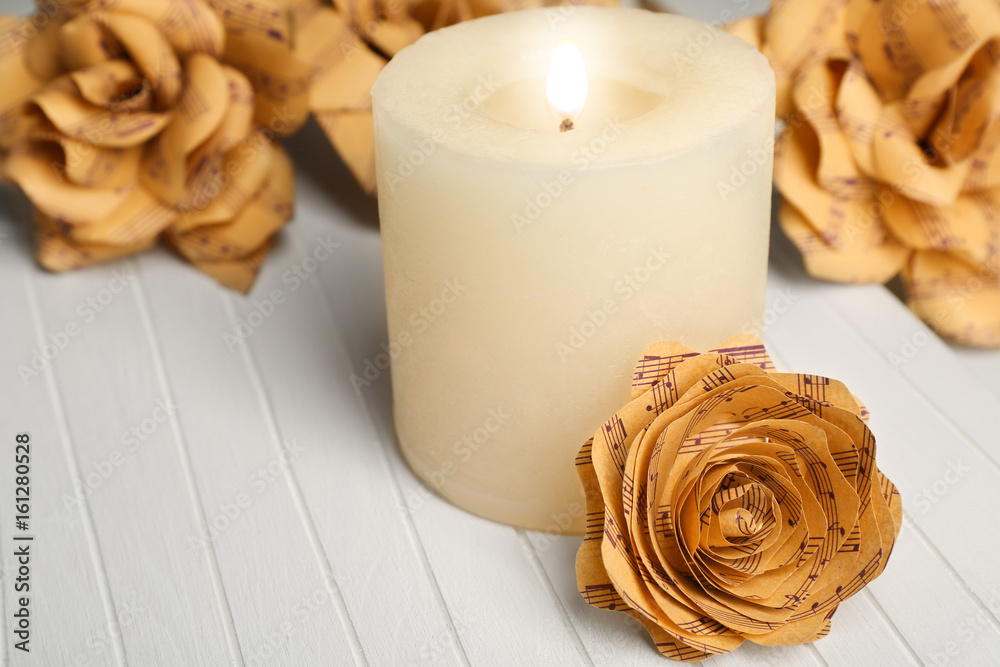 Fototapeta premium Beautiful roses made of music notes with candle on wooden table closeup