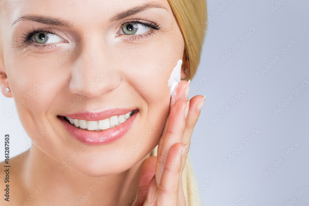 Obraz premium Happy woman applying cream on face looking away