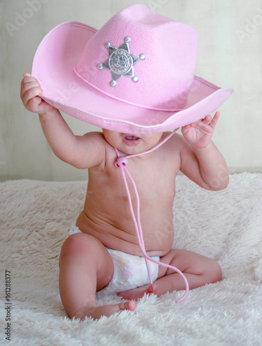 baby in a pink cowboy hat sitting in diapers on the couch