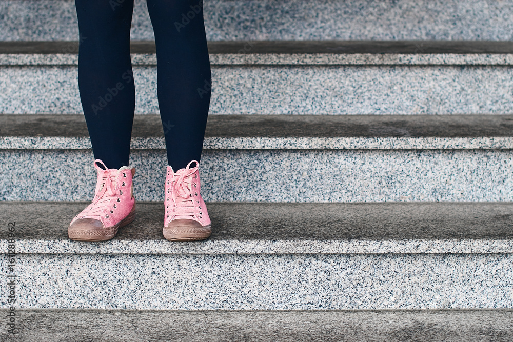 Woman legs in black leggings and pink sneakers standing on a stone stage Woman legs in black leggings and pink sneakers standing on a stone stage