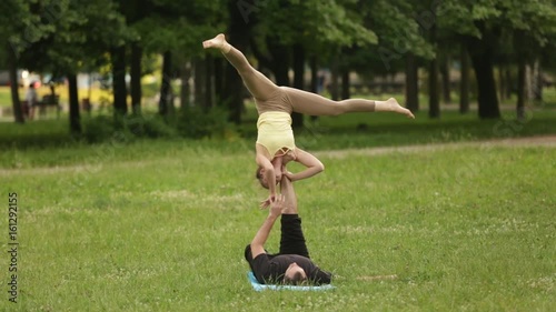 Beautiful couple practicing acro yoga. Young yoga instructors practice in a city park on green grass. Two successful young people perform acro yoga exercises. Man and a woman learn yoga at sunset. photo