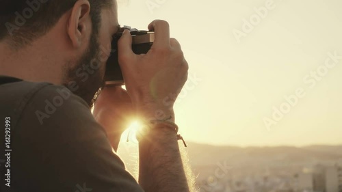 A young passionate photographer using a vintage film camera to photograph the city during sunset from a high angle photo