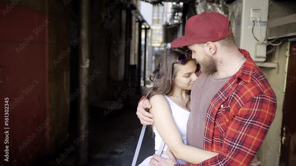Bearded adult man in shirt and cap holding the waist and hands of his beloved girlfriend. They are in the courtyard of the old town. Bearded adult man in shirt and cap holding the waist and hands of his beloved girlfriend. They are in the courtyard of the old town.