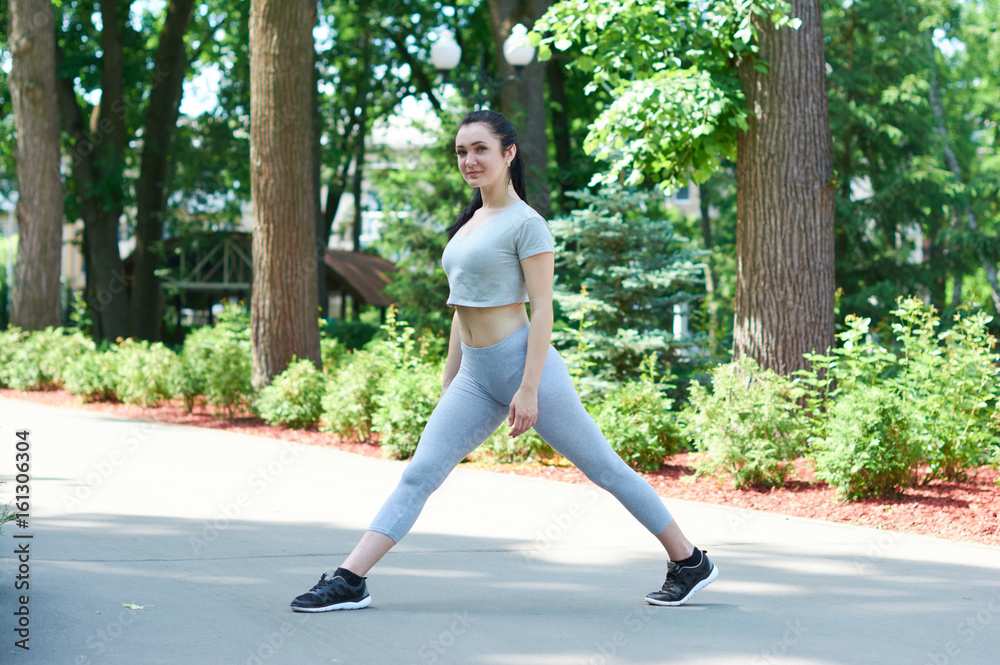Beautiful brunette girl exercising in a green park. Training in nature. A healthy lifestyle. Sportswear. Happy girl.