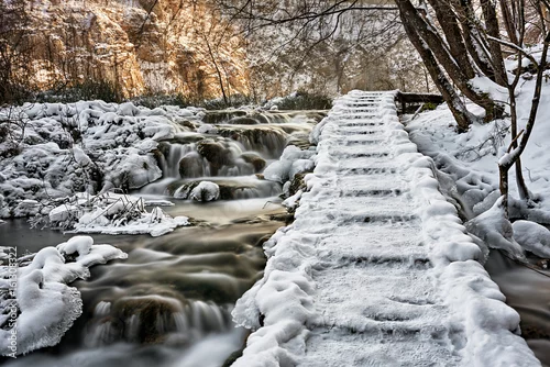 Obraz drewniana ścieżka koło wodospadu pokryta śniegiem i lodem