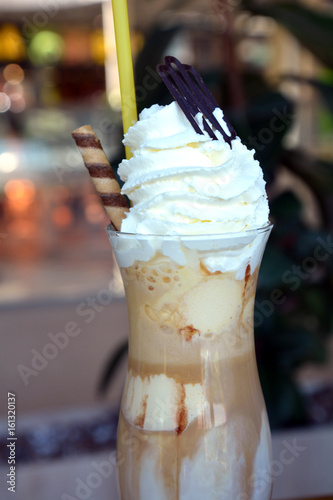 Glass cup of ice coffee with whipped cream on a wooden table.
